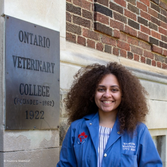 Living Planet Leader Youstina Makhlouf smiles while standing in front of a brick Ontario Veterinary College building wearing her "class of 2025" OVC blue coat.